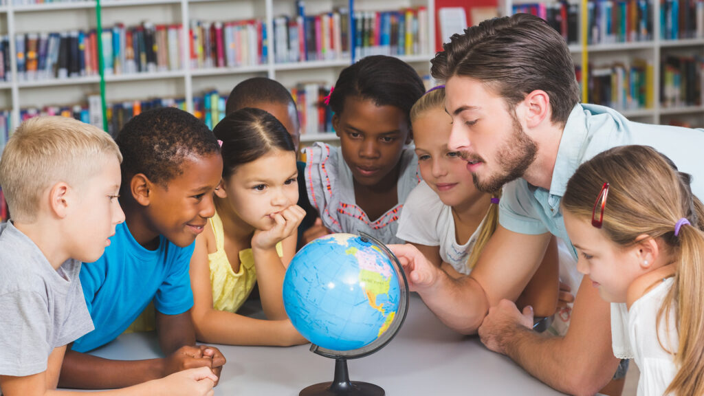 Mann schaut mit mehreren Kindern auf einen Globus während einer Lehrerfortbildung des Calleo-Instituts.